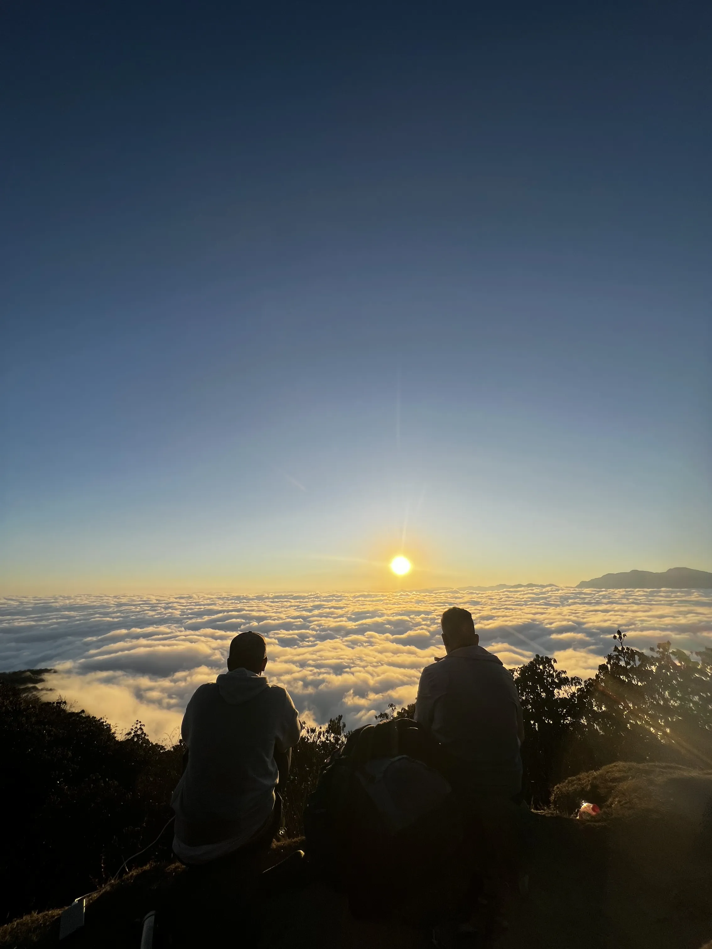Two trekkers watching sunset above the clouds